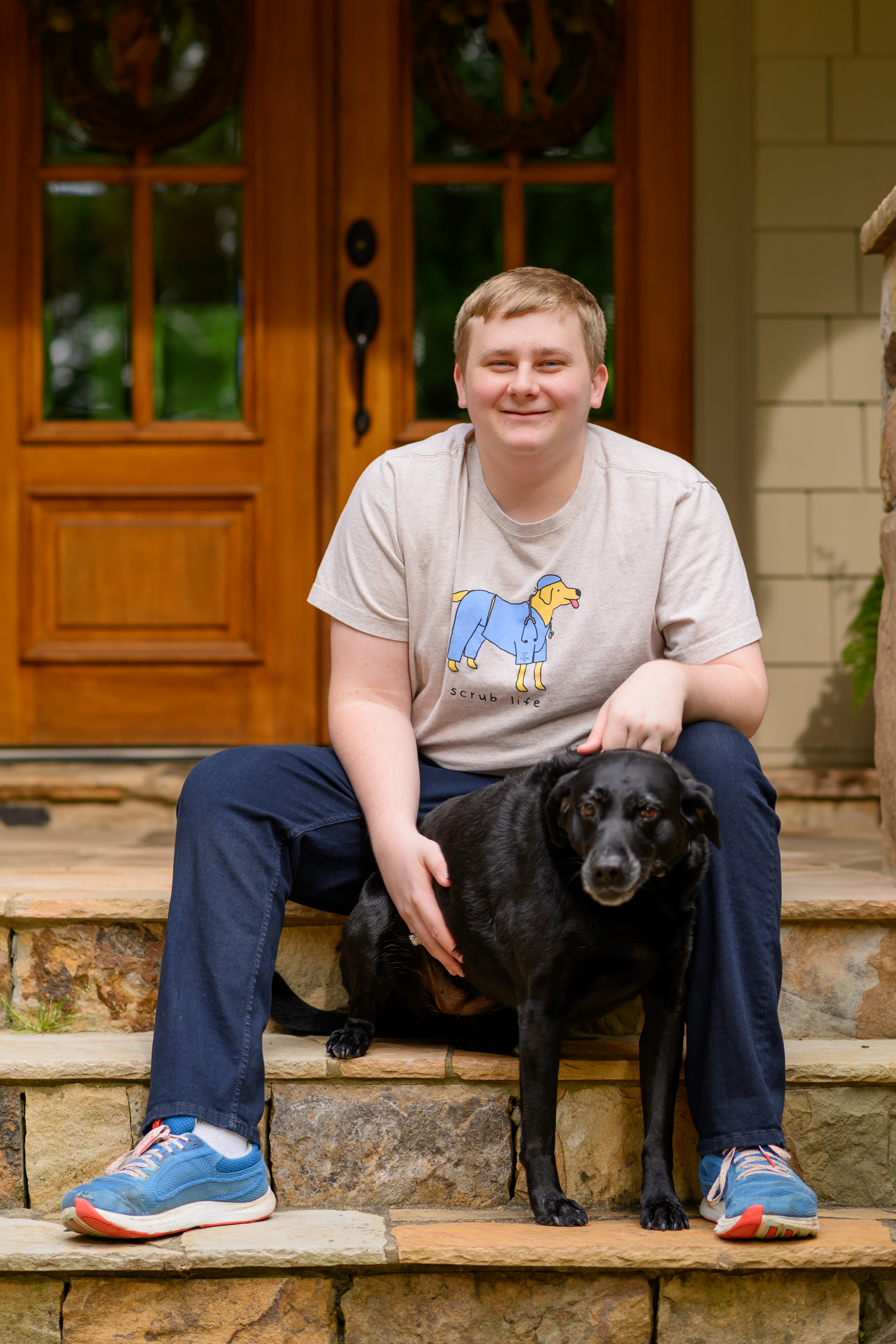 Reid sitting on porch steps with his dog Ellie, wearing a veterinary-themed shirt